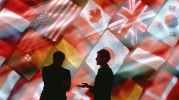 Two individuals talking, multinational flags in the background